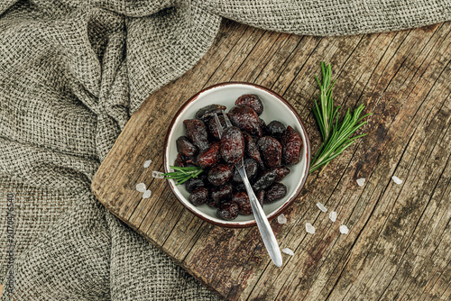 Black garlic cloves in oil with fresh rosemary branches and sea salt crystals in a ceramic bowl