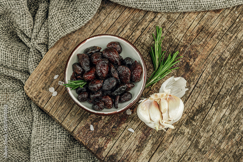 Black garlic cloves in oil with fresh rosemary branches and sea salt crystals in a ceramic bowl
