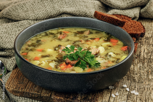 Traditional green sorrel soup with meat, eggs and vegetables in a black ceramic bowl. Rye bread