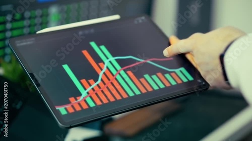 Hand holding tablet displaying stock market graph with fluctuating red and green bars and lines finance analysis data trading