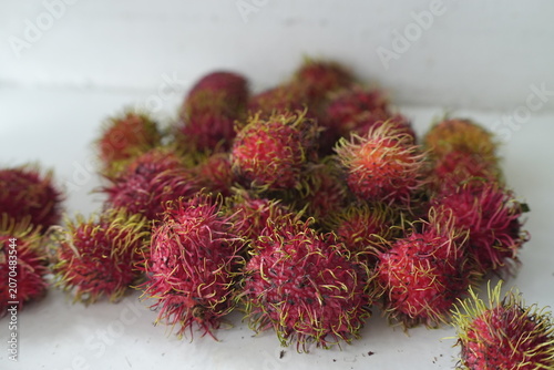 Fresh rambutans with vibrant red and pink skins are arranged together on a light background, showcasing their distinctive greenish-yellow soft spines. This image represents tropical freshness, natural