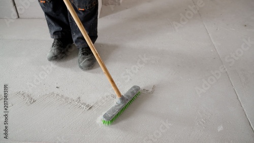 Worker sweeping concrete floor with green bristle broom in construction site