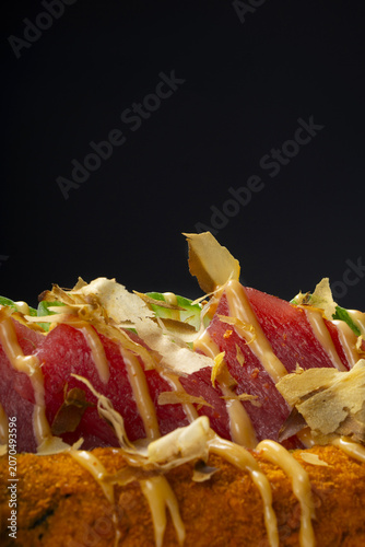 Tuna pieces with salad and sauce on a black background.