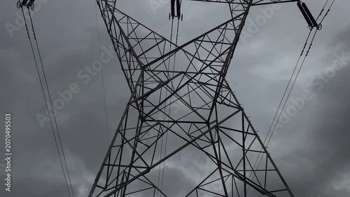 An industrial pylon cuts through dense, overcast clouds, capturing the grit of power crisis. The moody, storm-threatened sky evokes rain delays & structural strain, mirroring deep-seated social issues