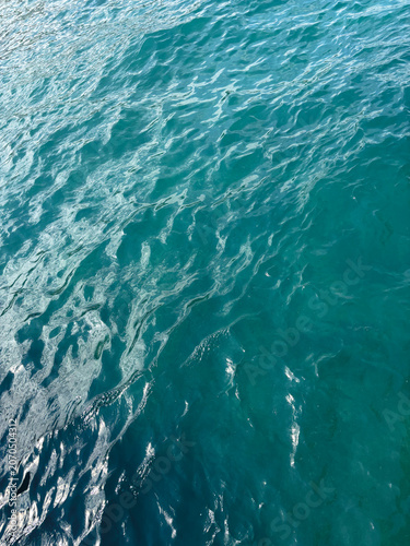 Abstract ocean water surface texture with soft sunlight reflections and gentle sea waves. Natural blue-green water background with ripples and shimmering patterns, calm marine atmosphere.