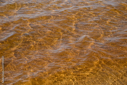 Sunlight interacting with ripples on water surface creating interesting patterns on lake Michigan beach.