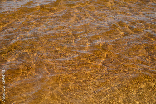 Sunlight interacting with ripples on water surface creating interesting patterns on lake Michigan beach.