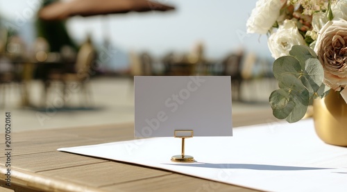 A blank place card sits on a wooden table with a floral arrangement