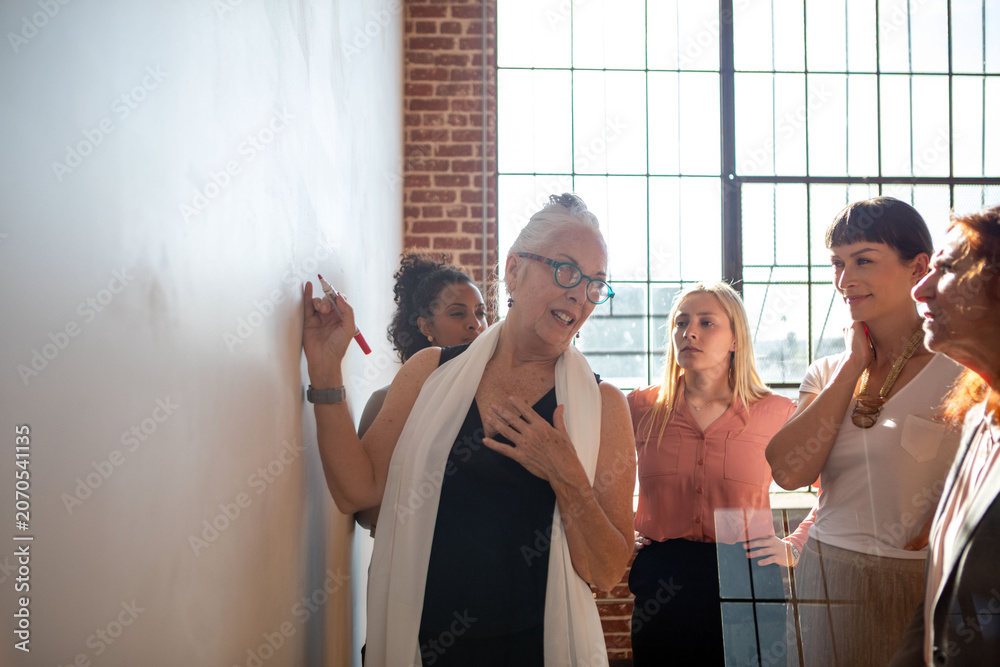 Fototapeta premium Diverse group of women collaborating at a whiteboard in a bright room.