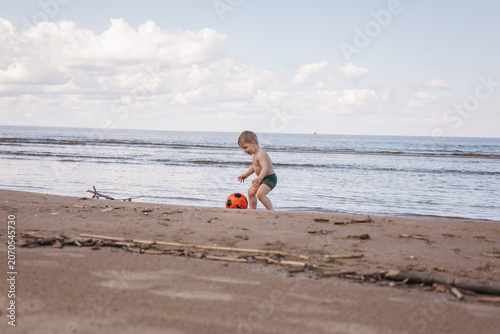 Toddler playing with a soccer ball on a sandy beach by the sea during summer vacation. Rear view of a child enjoying outdoor family leisure by the coast.