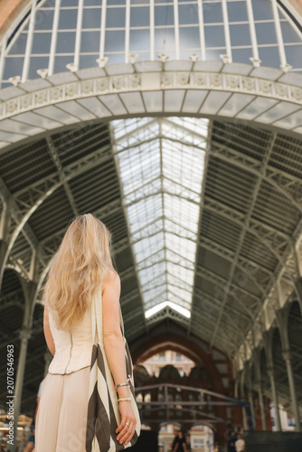 Young woman standing with her back under the historic Central Market building in Valencia, Spain. Female traveler exploring famous architecture and popular tourist destination during summer vacation.
