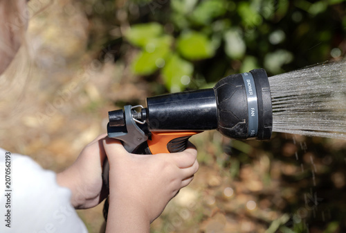 Children's hands hold a spray nozzle and water the plants in the garden