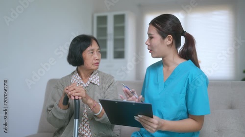 Young female doctor in scrubs visiting a senior woman at her home, explaining medical results from a clipboard and providing comfort and support during the consultation on a living room sofa