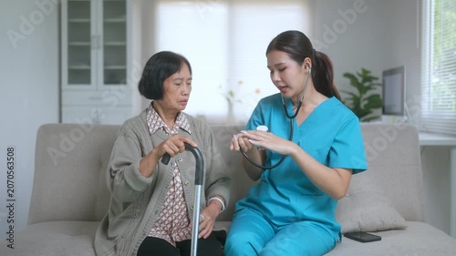 Female caregiver using a stethoscope to examine an elderly asian patient feeling unwell with chest pain during a home visit, providing medical assistance and checking her breathing
