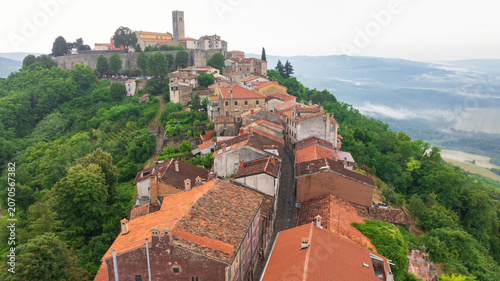 Famous medieval fortress town of Motovun stands proud on green hill in Istria. Aerial perspective shows ancient city walls, terracotta roofs, and mist rising from surrounding truffle forests.