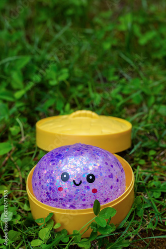 Purple glitter kawaii squishy dumpling toy in open yellow plastic steamer container on green grass