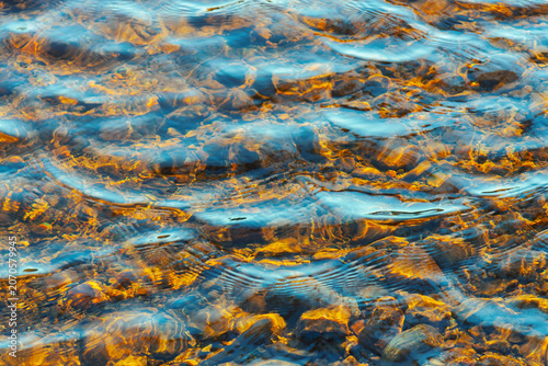 Foto Clear water ripples over golden stones abstract background