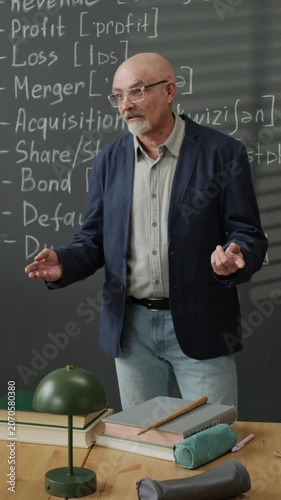 Vertical video of senior Caucasian male teacher explaining business terms written on blackboard during language class. Clip is perfect for promoting adult education and training courses