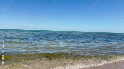 Calm summer seascape of the Black Sea with gentle waves rolling onto the shore under a clear blue sky. Crystal-clear water sparkles in the sunlight, creating a peaceful and relaxing atmosphere. Perfec