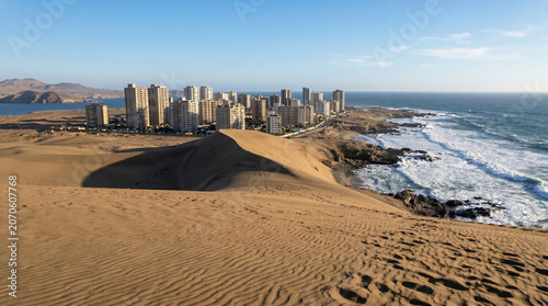 Desert dunes meet coastal city and ocean waves.