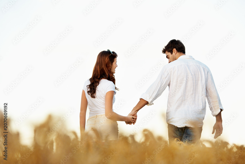 Obraz premium Couple, holding hands and back with walking outdoor, partner and support with care in nature. People, marriage and romantic stroll in meadow for healthy relationship, bonding and together with space