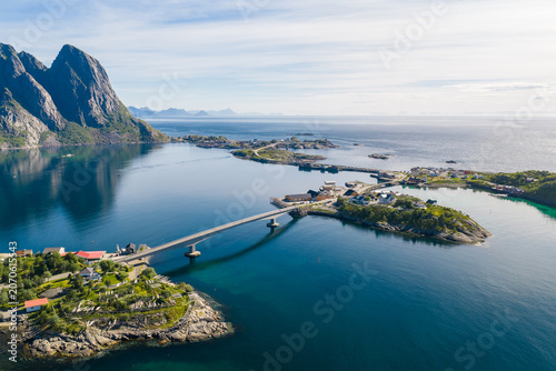 Fotografie Aerial view shows a sweeping bridge linking islets on a glassy fjord near Reinebringen in Lofoten, Norway