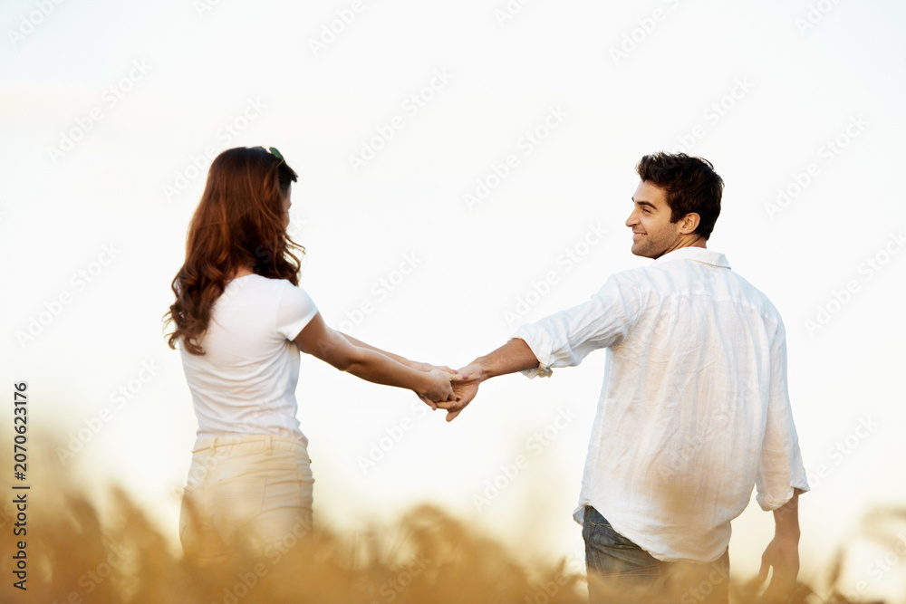 Obraz premium Couple, holding hands and walking outdoor in meadow, partner and support with care in nature. People, marriage and romantic stroll for healthy relationship, bonding and together with space for love