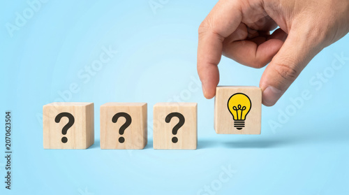 Hand replacing question mark light bulb on wooden blocks on blue background