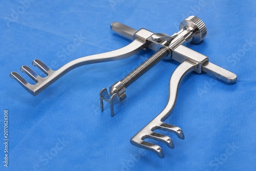 A stainless steel tissue retractor on a blue surgical drape under bright lights.
