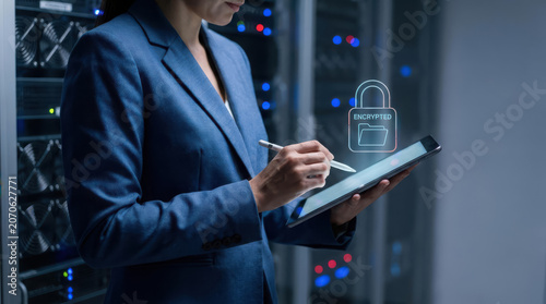 Businesswoman in blue suit holding tablet encrypted padlock icon on screen in server room