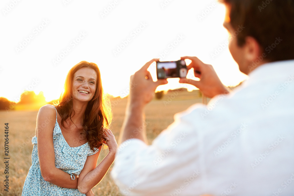 Obraz premium Woman, sunset and camera with couple in meadow, photography or memory of honeymoon. Female person, smile and nature with man and digital tech for picture taking, anniversary trip and relationship