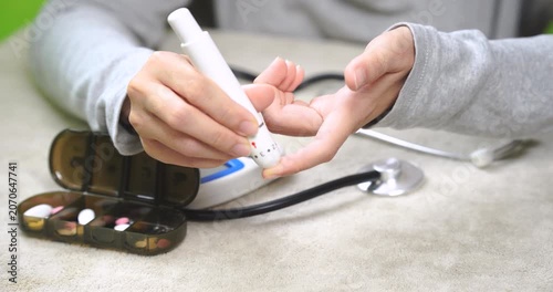 Close-up of a person performing a fingertip blood glucose test using a lancing device at home. Self health monitoring, diabetes management, wellness tracking, preventive care, and healthy lifestyle co
