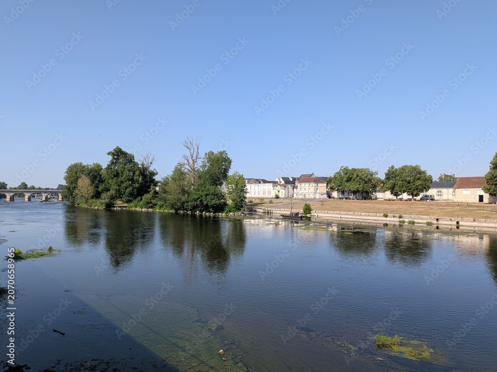 Fototapeta premium Scenic view of the Vienne river in Chatellerault with the historic Henri IV stone bridge and a traditional boat moored near the island, France.