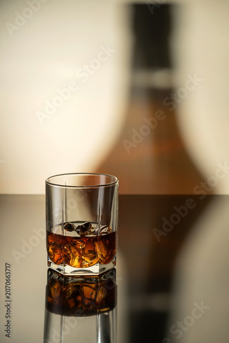 A glass of strong alcoholic drink in a glass with ice: vodka, cognac, tequila, scotch, brandy and whiskey, grappa, vermouth, rum. Light brown background with bottle shadow