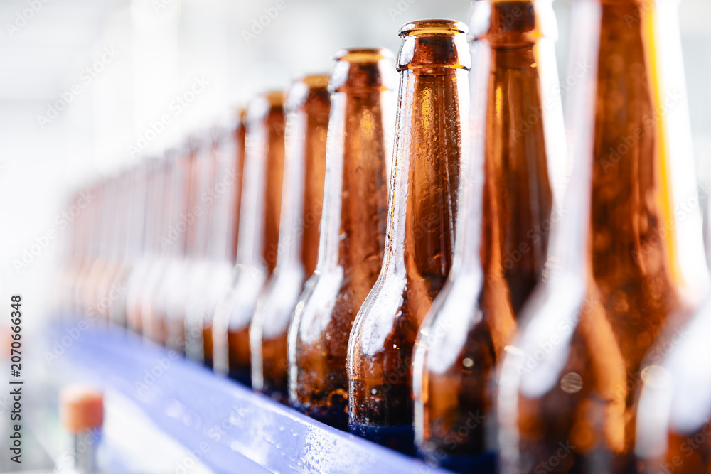 Obraz premium Rows of bottled beer in modern brewery factory setting, sunlight