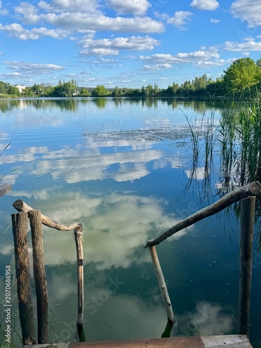 Obraz na plátně Quiet forest lake with wooden stairs leading to the water, reflecting clouds and surrounding trees on a calm day