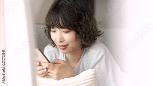 ソファに寝転んでスマートフォンを使う女性, Woman Using a Smartphone While Lying on a Sofa
