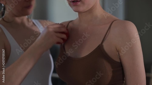 A female masseuse performs a massage on a female client's upper back and shoulders using a massage tool. The setting appears to be a well-lit indoor space, emphasizing relaxation and well-being