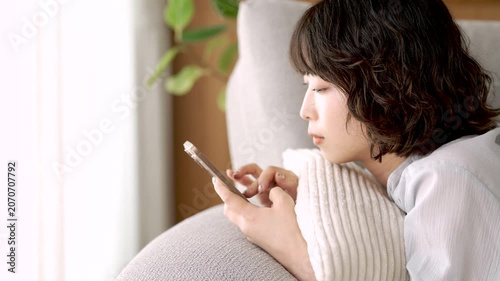 ソファに寝転んでスマートフォンを使う女性, Woman Using a Smartphone While Lying on a Sofa