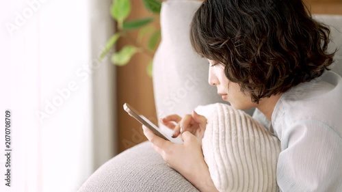 ソファに寝転んでスマートフォンを使う女性, Woman Using a Smartphone While Lying on a Sofa