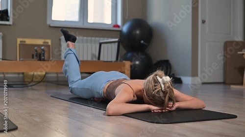 A woman in her twenties is doing floor exercises . She performs movements focused on core strength and flexibility while lying on a mat