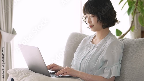 リビングのソファでノートパソコンを使う女性, Woman Using a Laptop on a Sofa in the Living Room