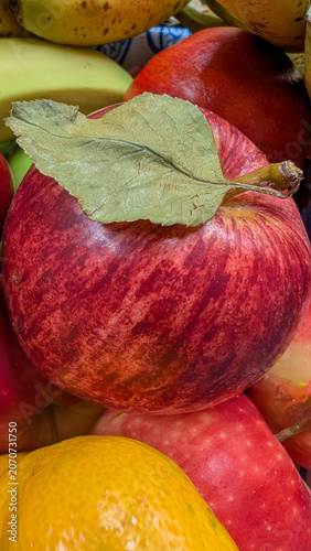A close-up of a red apple with a green leaf nestled among other bright fruits, showcasing freshness and variety