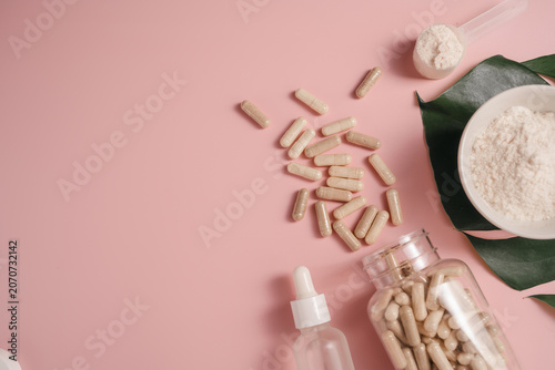 Collagen powder, food supplements capsules and serum bottle on monstera leaf over pink background