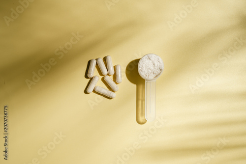 Collagen powder scoop and dietary supplement capsules on yellow background, flat lay with copy space