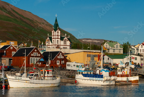 Fotografie Fishing boats in Húsavík Harbor Iceland with the iconic Húsavík Church colorful
