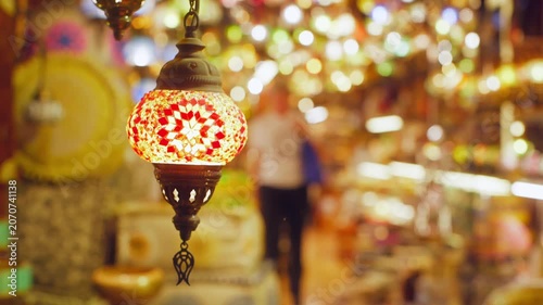 Ornate red, white, yellow mosaic glass lamp hangs in busy traditional market with warm blurred background lights, showcasing handcrafted Middle Eastern decor.