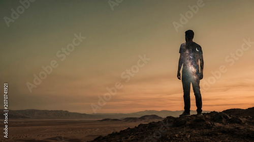 Silhouetted figure stands alone atop a rocky hill. Dusk bathes the desert in warm, fading light. Remote and vast, the landscape stretches to distant hills