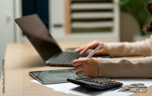 Side view close up hands of business woman use tablet pen to take note while use the other hand to type some work on laptop with the calculator and coins are in front of hands.