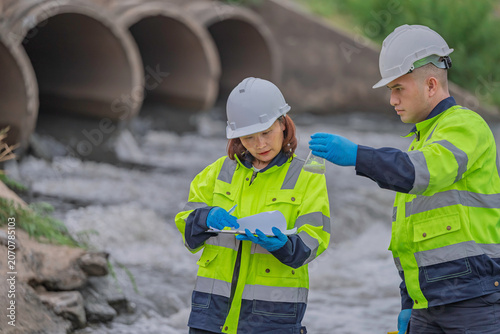 Environmental engineers collecting water samples for laboratory analysis and quality control monitoring near industrial drainage pipes to ensure safety and ecological sustainability standards.